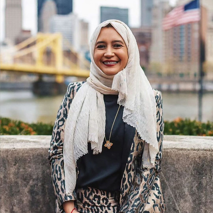 a headshot of a smiling woman wearing a cheetah print suit and a beige head covering