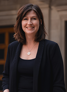 A white woman wearing a black top and black cardigan