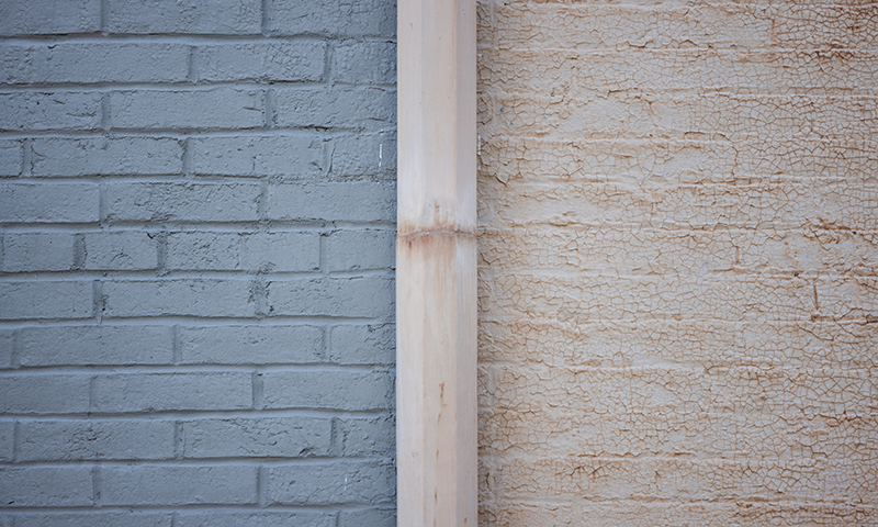 a brick wall that is half painted a deteriorating yellow color and half painted a fresh coat of green/gray paint