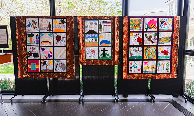 three patchwork quilts on display in a window-filled room